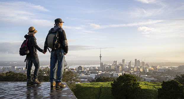 A couple stand, holding hands, on a platform overlooking Auckland city